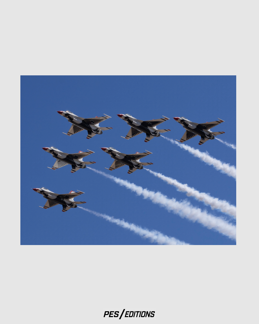 The United States Air Force Thunderbirds flying in a precise 6-ship diamond formation against a solid blue sky, leaving long, crisp white smoke trails in their path.