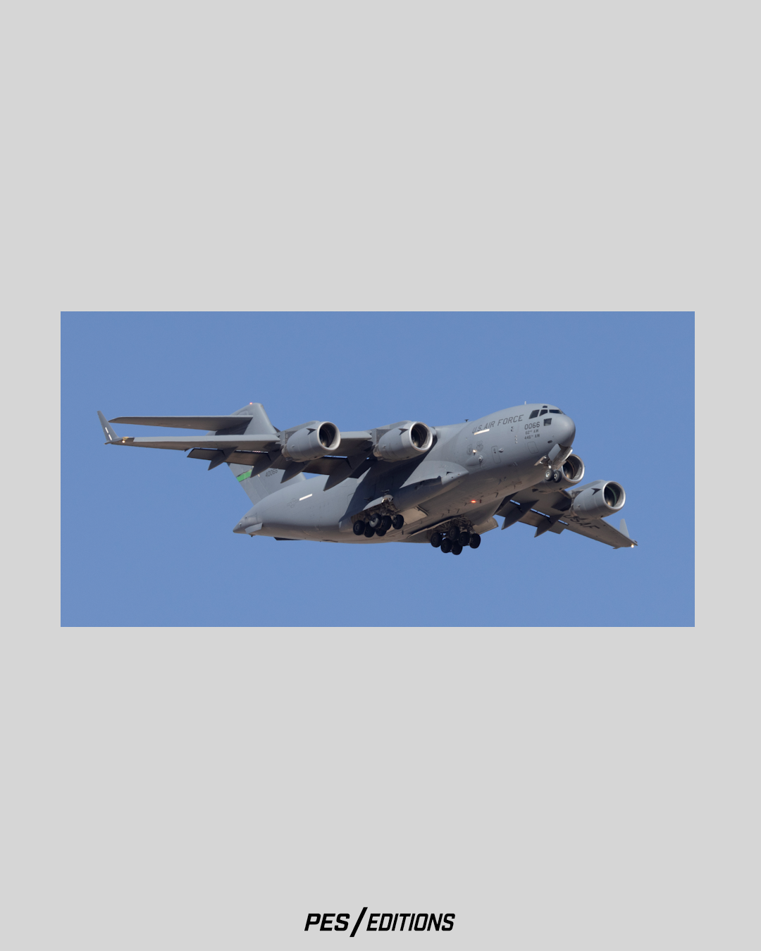 Dynamic three-quarter nose perspective of a U.S. Air Force C-17A Globemaster III heavy logistics transport jet descending against a flawless blue sky, captured on location at Nellis Air Force Base by Phil Schmauder.