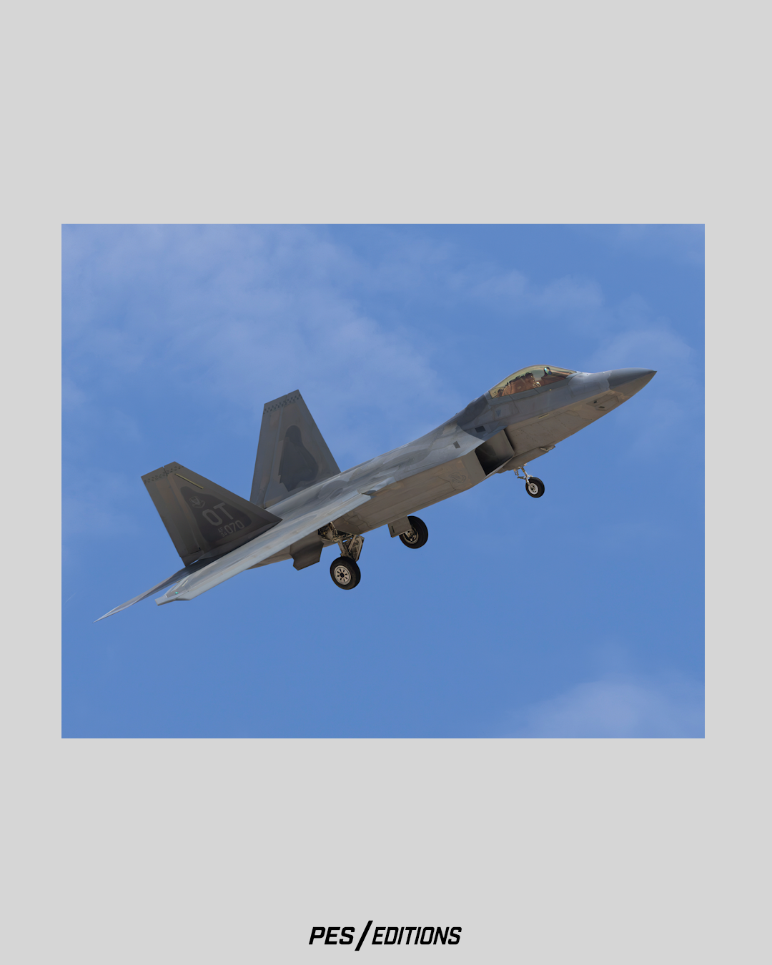 A low-angle profile photograph of an F-22 Raptor stealth fighter jet flying against a blue sky with light clouds, captured with its landing gear deployed as it prepares for approach.