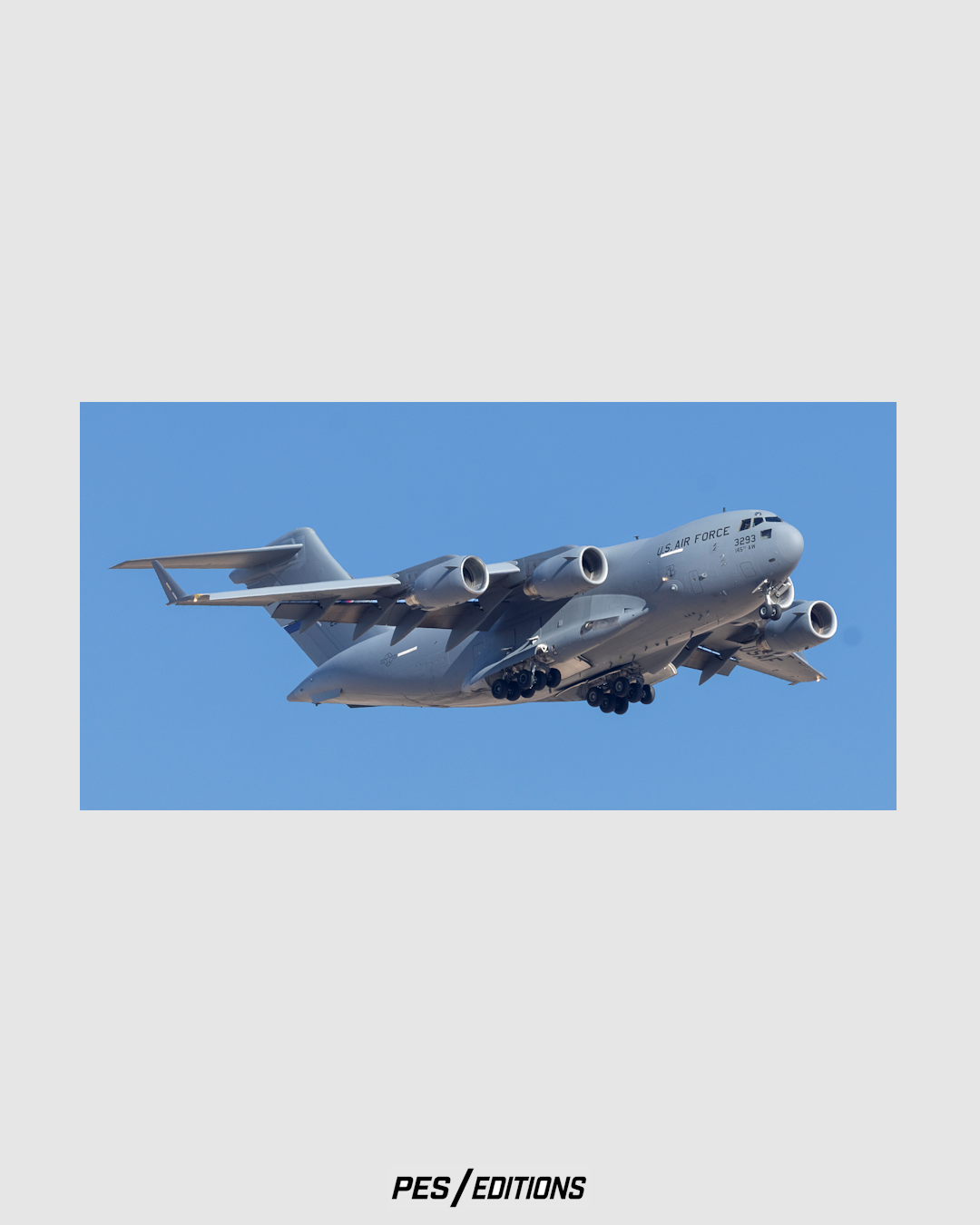 A powerful, close-up photograph of a large U.S. Air Force C-17A Globemaster III military transport aircraft on landing approach against a pale blue sky.