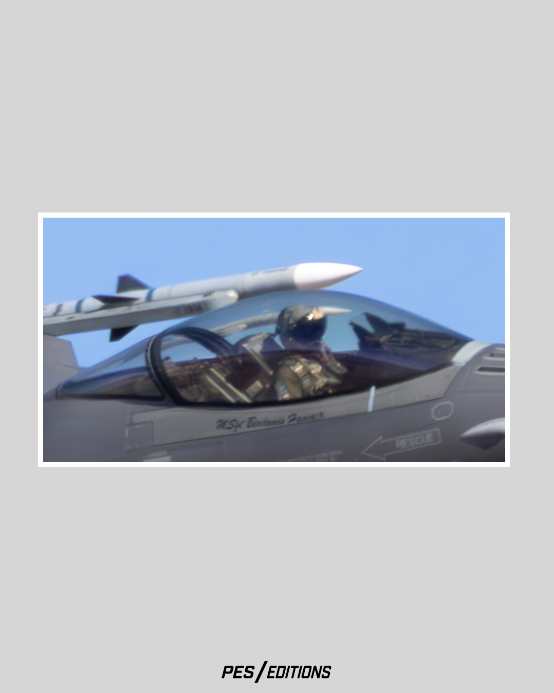 An extreme close-up of an F-16 pilot inside the cockpit. The bubble canopy reflects the sky while a training missile sits on the wingtip.