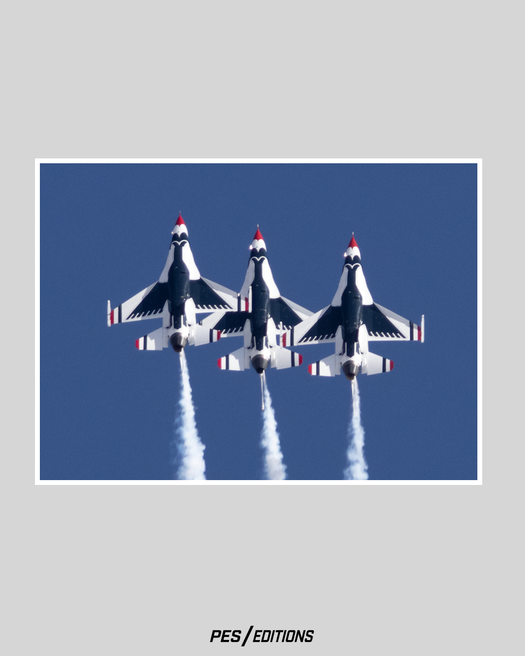 Three USAF Thunderbirds climbing in formation with smoke on. The underside view reveals the iconic blue bird logo painted on the F-16s.