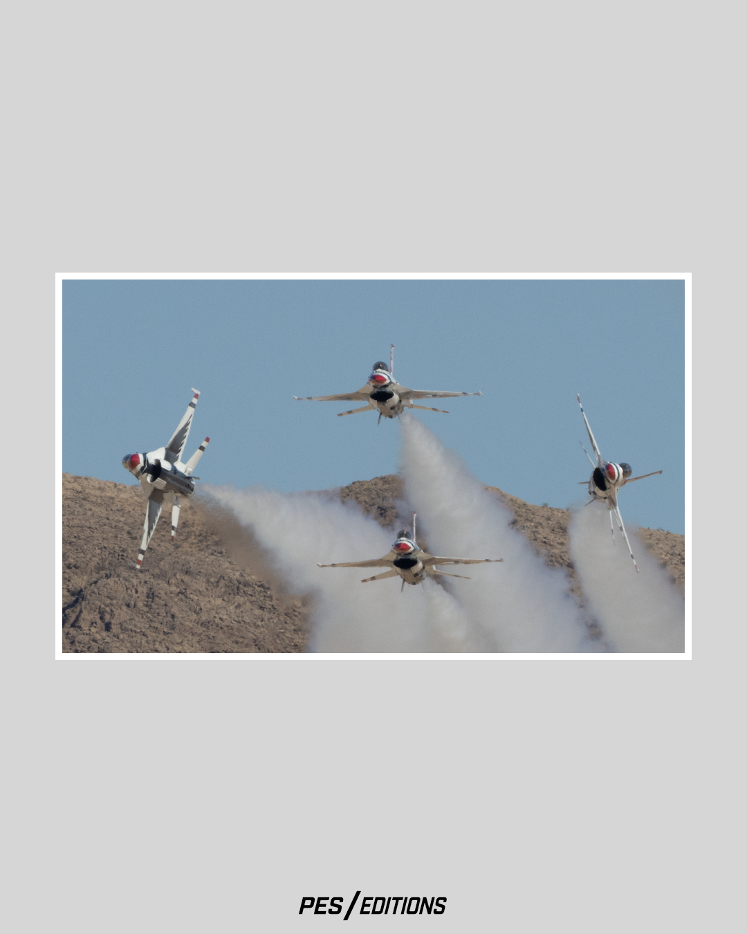 Four U.S. Air Force Thunderbirds F-16 fighter jets peeling away from a tight formation, leaving thick white smoke trails against a backdrop of rugged mountains and blue sky.