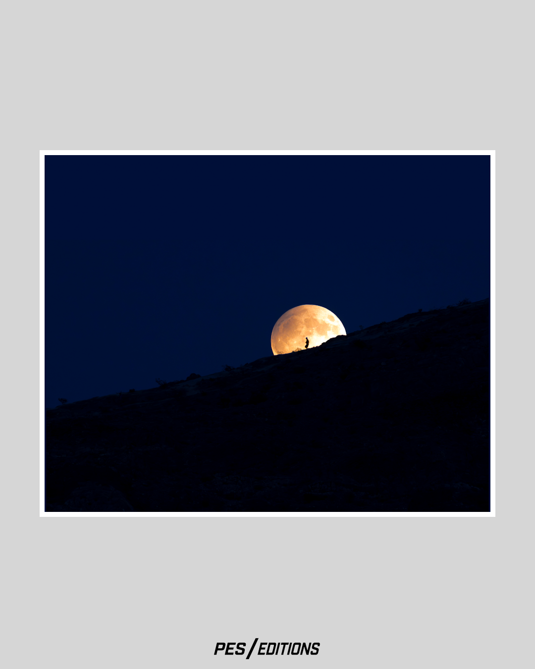 Silhouette of a lone hiker walking along a dark mountain ridge, backlit by a massive, detailed full moon rising against a deep blue night sky.